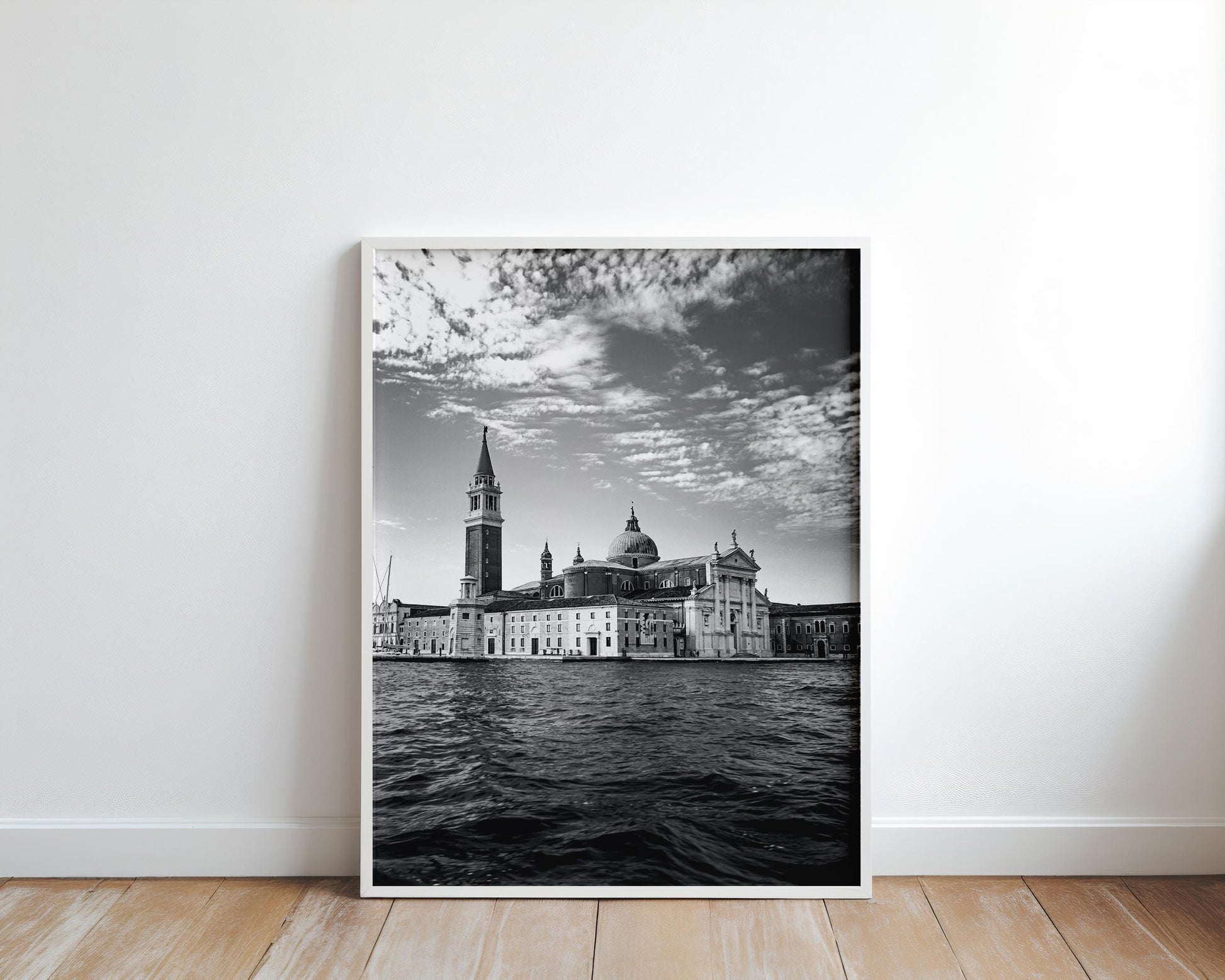 Large black-and-white Venice photo in a white frame leaning against a clean white wall on a wooden floor.