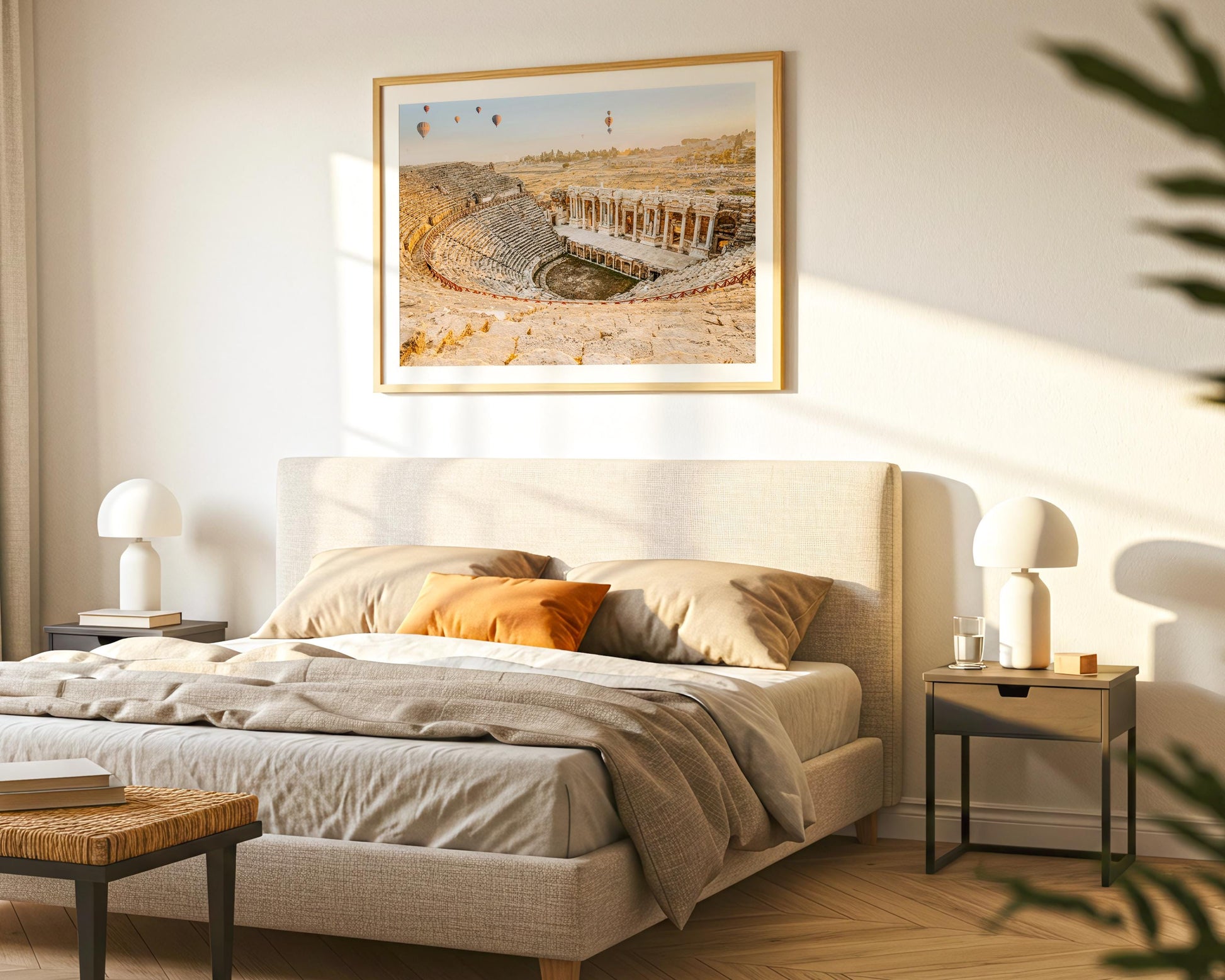 Minimal bedroom scene with a framed Hierapolis print above the bed, sunlight casting soft shadows, and simple bedside lamps on both sides.