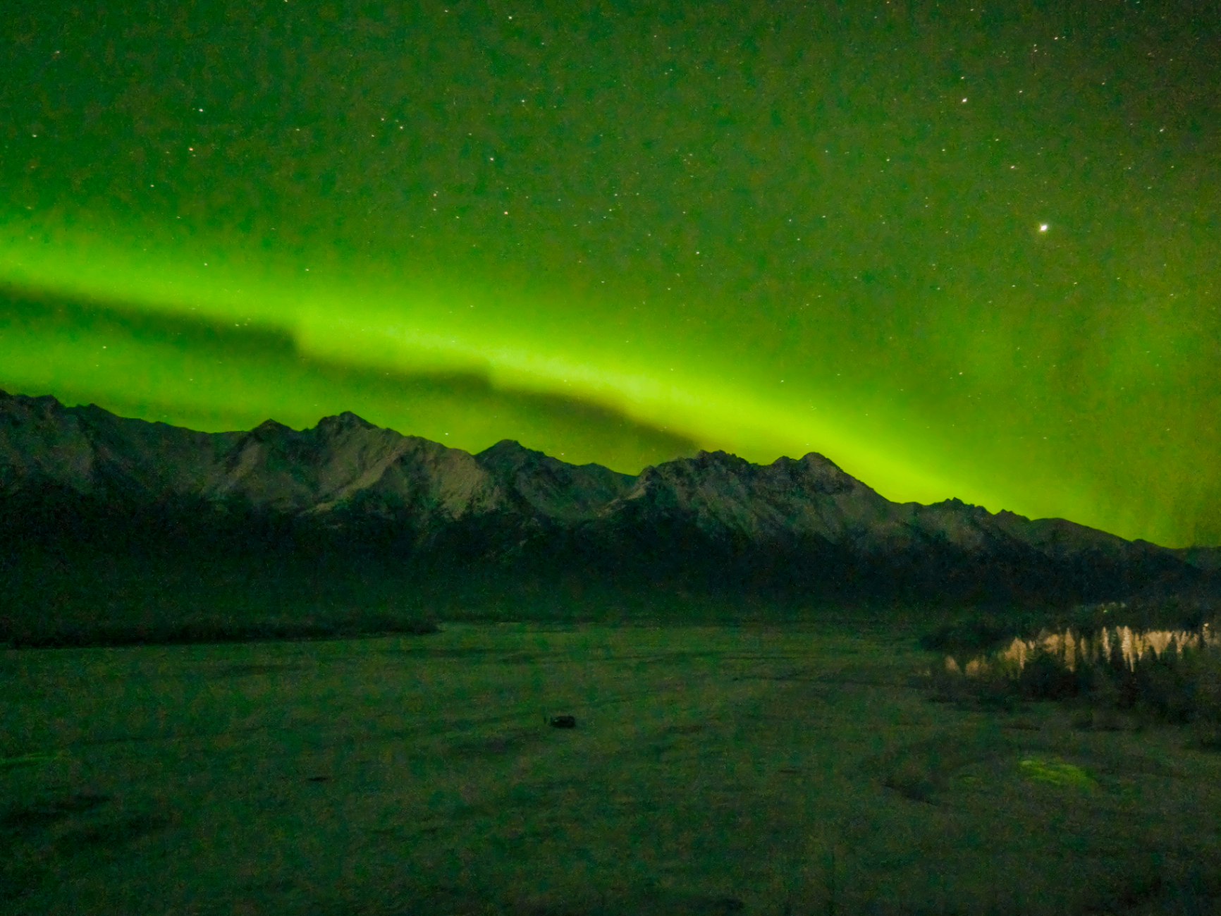 Green aurora curtains above snow-capped Alaskan mountains